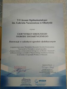 Przedstawia dyplom, który otrzymała szkoła, na którym napisano: VI Liceum Ogólnokształcące im. Gabriela Narutowicza w Olsztynie otrzymuje CERTYFIKAT SZKOLNEGO OGRODU DYDAKTYCZNEGO Innowacje w szkolnym ogrodzie dydaktycznym zorganizowany przez Warmińsko – Mazurski Ośrodek Doskonalenia Nauczycieli w Olsztynie w ramach projektu „Zmiana klimatu a różnorodność biologiczna na Warmii i Mazurach, dofinansowanego ze środków Wojewódzkiego Funduszu Ochrony Środowiska i Gospodarki Wodnej w Olsztynie. Na dyplomie złożono podpisy organizatorów.