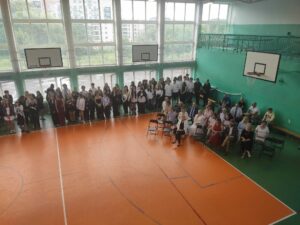 Widok stojących uczniów i siedzących nauczycieli