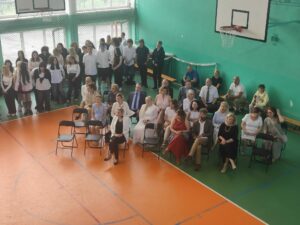 Widok stojących uczniów i siedzących nauczycieli