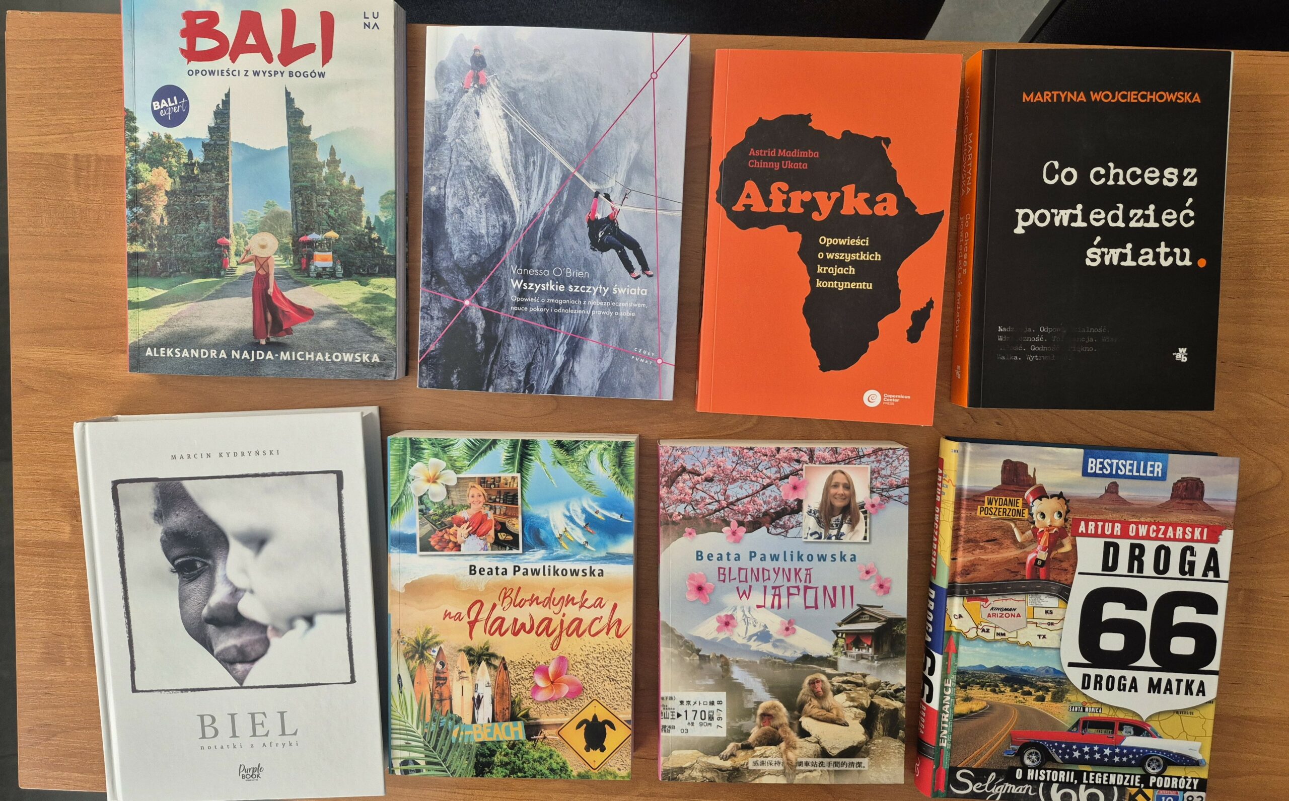 Zdjęcie przedstawia książki podróżnicze, między innymi: „Biel”, „Blondynka na Hawajach”, „Blondynka w Japonii”, „Droga 66”, „Co chcesz powiedzieć światu”, „Bali. Opowieści z wyspy bogów”.