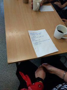 Przedstawia leżącą na stoliku kartkę, a niej napisany jest wiersz awangardowy. Obok stroi kubek z kawą.